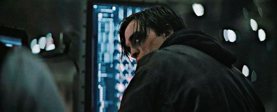 An screenshot of the movie The Batman, as Bruce Wayne looks back over his shoulder in the batcave